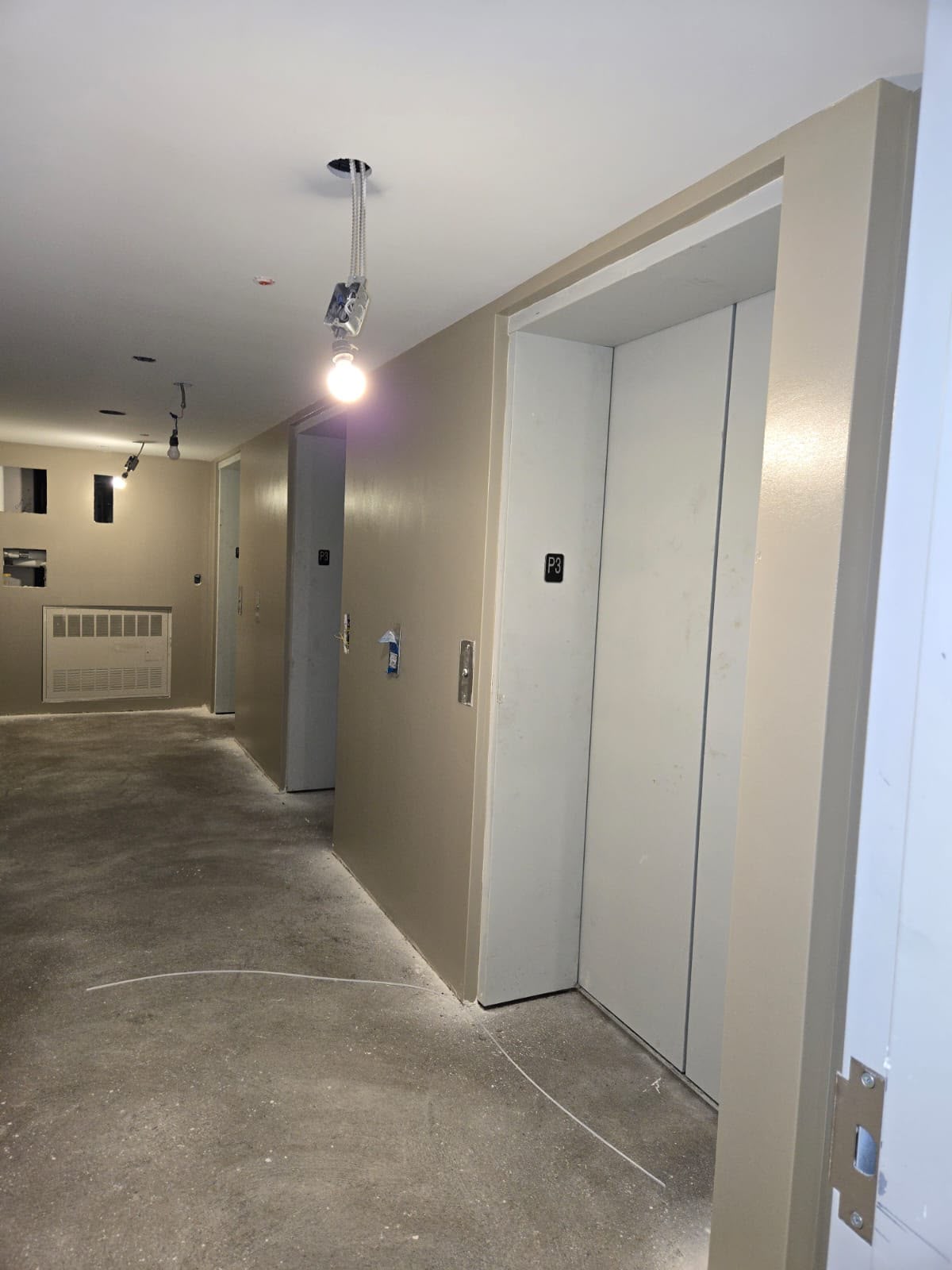 Parking-level elevator lobby before painting — bare beige walls and concrete floor