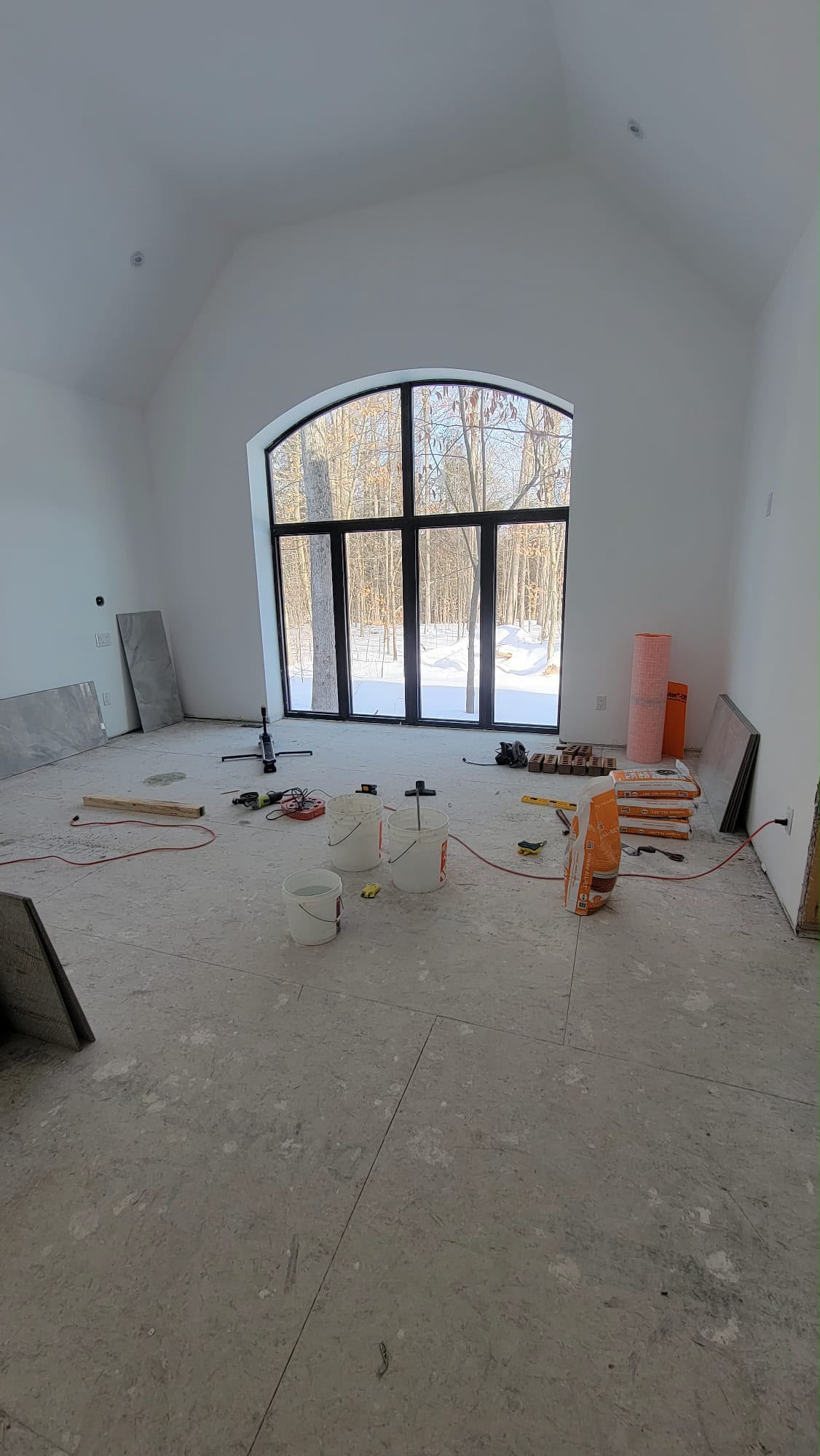 Large residential great room with arched window during construction and painting