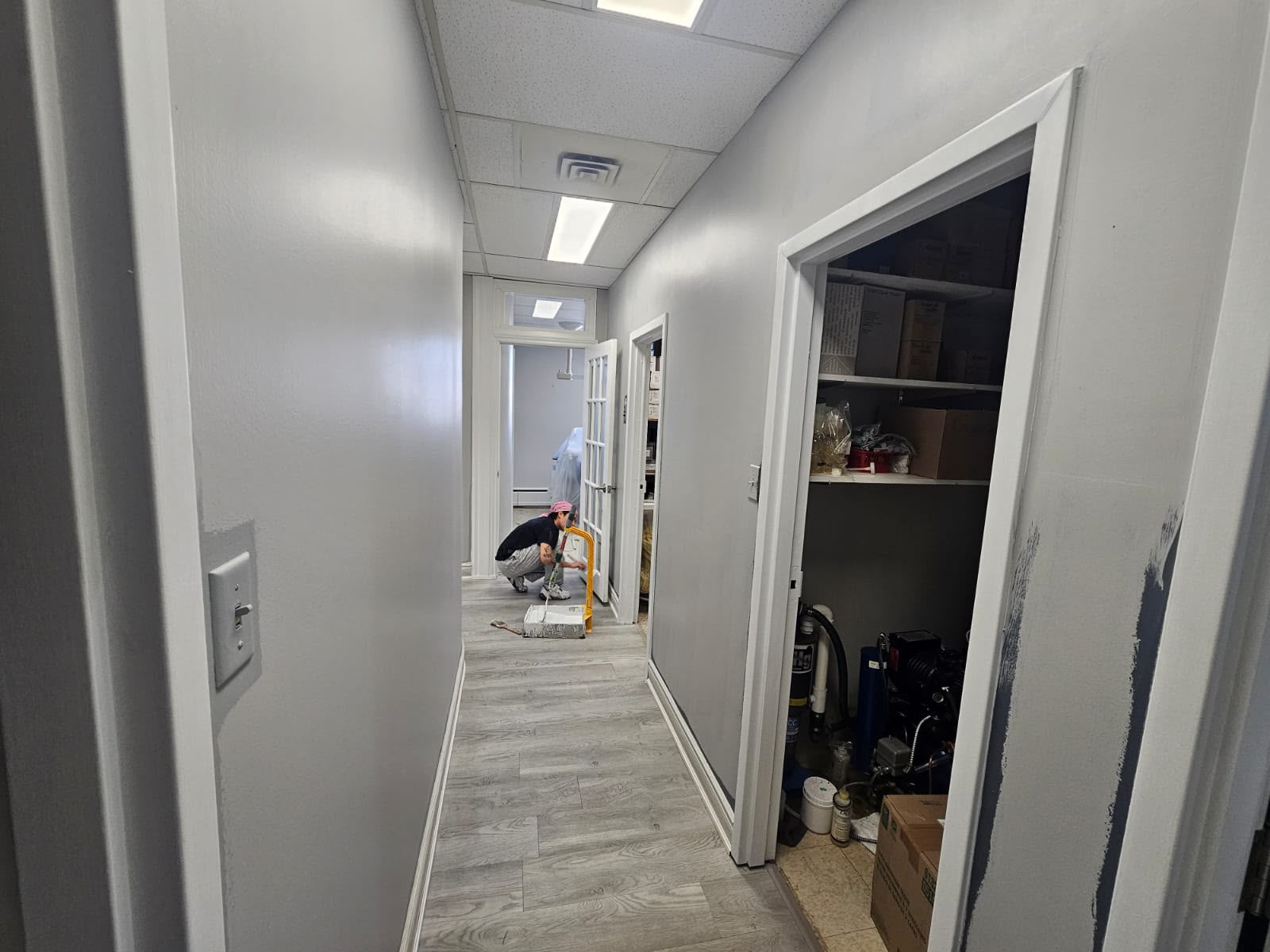 Painter working in a commercial office corridor — grey walls being applied